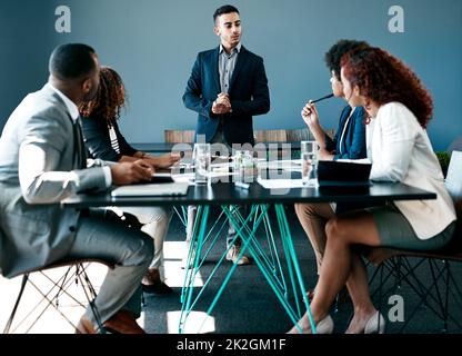 Er hat das Wort. Eine kleine Aufnahme eines hübschen jungen Geschäftsmannes, der sich während einer Sitzung im Sitzungssaal an seine Kollegen wendet. Stockfoto