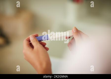 Überprüfung der Ergebnisse ihres Schwangerschaftstests. Ausgeschnittene Aufnahme einer unkenntlichen Frau, die zu Hause im Badezimmer einen Schwangerschaftstest abhält. Stockfoto