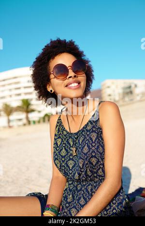 Etwas Vitamin D bekommen eine kurze Aufnahme einer attraktiven jungen Frau in legerer Kleidung, während sie alleine am Strand sitzt und die Sonne genießt. Stockfoto