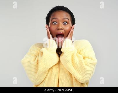 Ich kann meinen Augen nicht glauben. Aufnahme einer jungen Frau, die überrascht vor grauem Hintergrund posiert. Stockfoto