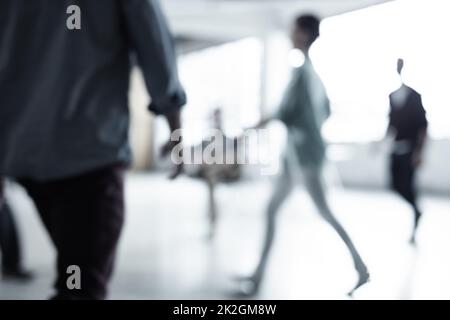 Die Unternehmenswelt steht nie still. Eine kurze Aufnahme einer Gruppe von Geschäftsleuten, die durch ein Büro gehen. Stockfoto