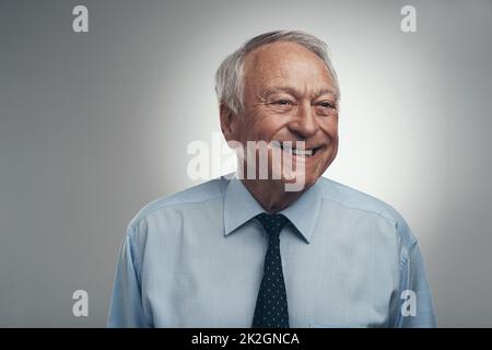 Glück ist nie etwas, das aus der Mode kommt. Foto eines Geschäftsmanns, der tagsüber allein vor grauem Hintergrund im Studio steht. Stockfoto