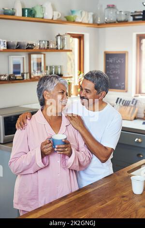 Wie dein Kaffee-Honig. Aufnahme eines fröhlichen älteren Paares, das sich gegenseitig hält, während es sich in die Augen schaut und zu Hause tagsüber Kaffee trinkt. Stockfoto