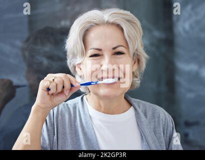 Ich habe immer noch alle meine Zähne, weil ich mich gut darum kümmere. Aufnahme einer älteren Frau, die zu Hause ihre Zähne putzt. Stockfoto