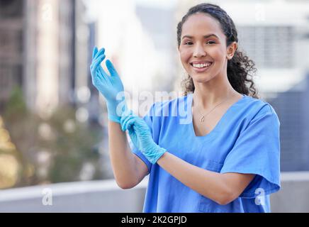 Vorbereitung auf eine Untersuchung. Aufnahme einer jungen Ärztin, die vor einem Stadthintergrund Handschuhe anlegt. Stockfoto