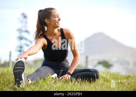 Stellen Sie sicher, dass Sie immer mit einer wirklich guten Dehnung beginnen. Aufnahme einer sportlichen jungen Frau, die ihre Beine während des Trainings im Freien streckt. Stockfoto