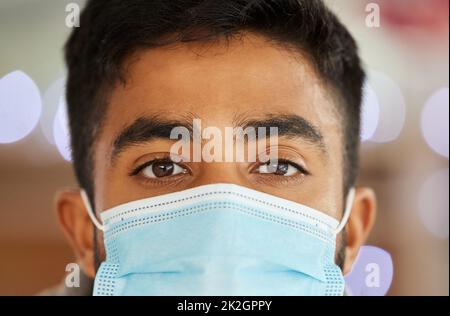 Diese Maske wurde zu meinem und zu Ihrem Schutz gemacht. Porträt eines jungen Mannes, der eine chirurgische Gesichtsmaske in Innenräumen trägt. Stockfoto