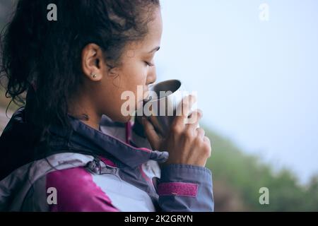 Kaffeepausen sind auf Wanderungen am frühen Morgen erforderlich. Kurze Aufnahme einer attraktiven jungen Frau, die während ihrer frühen Morgenwanderung Kaffee trinkt. Stockfoto