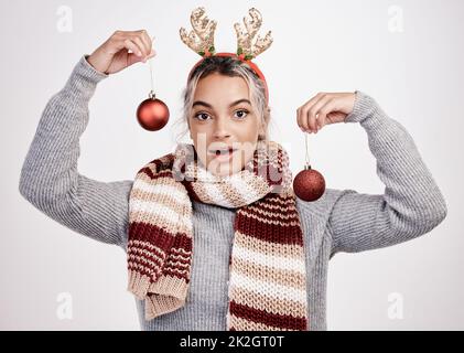 Lassen Sie uns dekorieren. Studioporträt einer attraktiven jungen Frau, die in weihnachtlicher Kleidung Kugeln in die Hand hält. Stockfoto