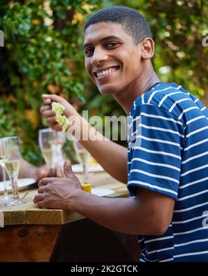 Ich bin am glücklichsten, wenn mein Bauch voll ist. Aufnahme eines jungen Mannes, der mit seinen Freunden in einem Café im Freien zu Mittag gegessen hat. Stockfoto