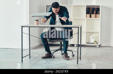 Dieser Laptop ist zu langsam für mich. In voller Länge ein hübscher junger Geschäftsmann, der allein im Büro sitzt und seinen Laptop vor Wut wirft. Stockfoto