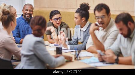 Um den Sitzungstisch. Eine kurze Aufnahme einer großen Gruppe von Geschäftsleuten, die während eines Meetings an einem Tisch im Sitzungssaal sitzen. Stockfoto