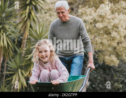 Lass dein inneres Kind niemals alt werden. Aufnahme eines entzückenden kleinen Mädchens, das Spaß mit ihrem Großvater in einem Garten hat. Stockfoto