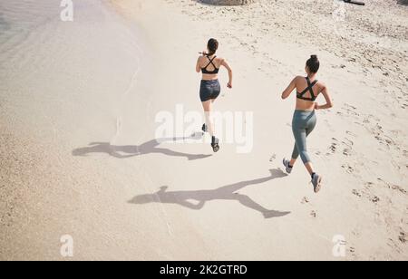 Hinterlassen ihre Spuren auf der Strecke. High-Angle-Aufnahme zweier nicht erkennbarer sportlicher junger Frauen, die für einen Lauf am Strand unterwegs sind. Stockfoto