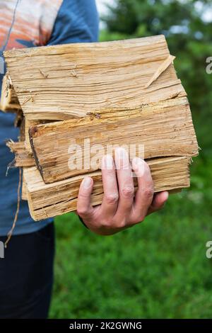 Die Hände des Mannes halten Feuerholz. Ein nicht erkennbarer Mann trägt Feuerholz zum Haus, um einen Kamin anzuzünden. Rustikale Landschaft Hintergrund. Stockfoto