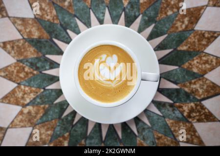 Weiße Tasse Cappuccino-Kaffee mit herzförmigem Schaum auf einem wunderschönen Tisch. Blick von oben. Stockfoto