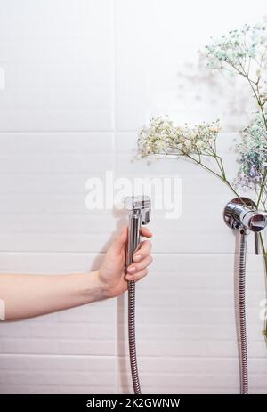 Hygiene- und Reinheitskonzept. Neue hygienisch verchromte Dusche in der Hand vor weißem Fliesenhintergrund. Badezimmer. Stockfoto