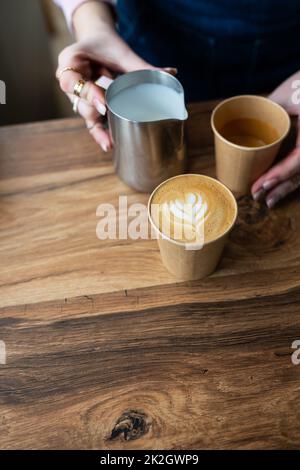 Der Prozess der Zubereitung eines Barista Cappuccino mit einem wunderschönen Muster auf dem Schaumstoff in einem Eco-Craft-Glas. Kaffee zum Mitnehmen. Stockfoto