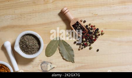 Mörser und Stößel mit Kräutern und Pfefferkörnern auf einem Holztisch Stockfoto