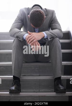 Es sollte sich nicht so herausstellen: Ein verzweifelter Geschäftsmann, der nach dem Abschuss auf einer Treppe gebeugt saß. Stockfoto