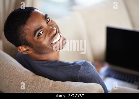 Ein schöner junger Mann, der seinen Laptop benutzt, während er sich zu Hause entspannt. Stockfoto