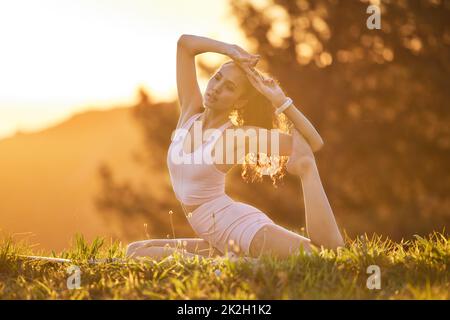 Yoga ist der Schlüssel zu einem gesunden Leben. Ganzkörperaufnahme einer attraktiven jungen Frau, die an einem sonnigen Morgen im Freien Yoga praktiziert. Stockfoto