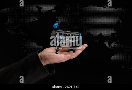 Die Hand eines Mannes hält einen Miniatur-Einkaufswagen auf dunklem Hintergrund, Konzept des Beginns des weltweiten Verkaufs Stockfoto