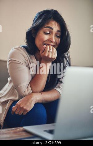 Ihre Nerven sind abgeschossen. Aufnahme einer jungen Frau, die sich bei der Arbeit an einem Laptop zu Hause die Nägel beißt. Stockfoto