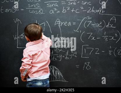 Mathe beherrschen. Aufnahme eines Jungen mit einer Tafel voller mathematischer Gleichungen. Stockfoto