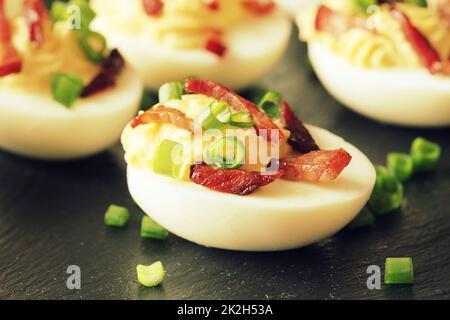 Gefüllte Deviled-Eier mit Speck auf schwarzem Hintergrund Stockfoto