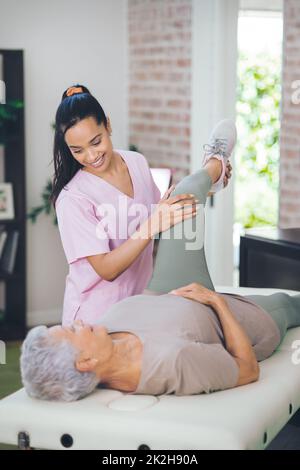 Zusammen, waren besser. Aufnahme einer älteren Frau, die während einer Sitzung mit einem Physiotherapeuten im Inneren leichte Übungen macht. Stockfoto