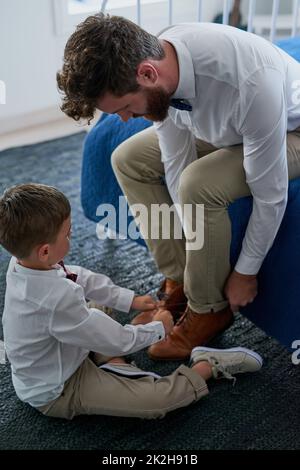 Helfen Sie dem Vatel, seine Schnürsenkel zu binden. Kurzer Schuss eines entzückenden kleinen Jungen, der zu Hause Schnürsenkel seines Vaters bindet. Stockfoto