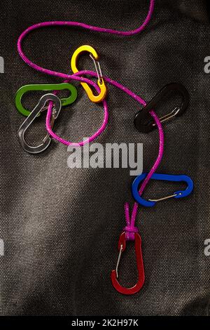 Farbenfrohe Karabiner-Accessoires an einem kleinen violetten Seil mit dramatischer, dezenter Beleuchtung. Dieses Werkzeug ist nicht zum Klettern geeignet Stockfoto