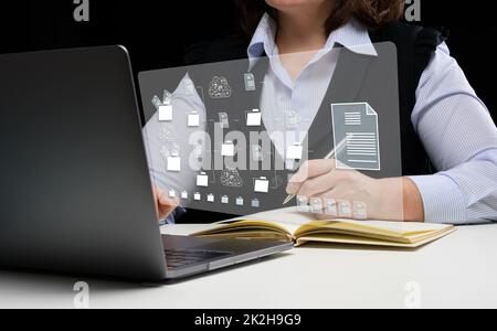 Frau sitzt an einem Tisch und arbeitet mit einem Laptop. Dokumentenmanagementsystem (DMS). Software zur Automatisierung der Archivierung und effizienten Verwaltung von Informationsdateien Stockfoto