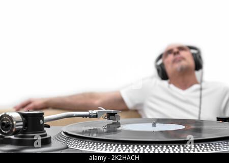 Vinyl-Schallplatte auf dem Player vor dem Hintergrund eines verschwommenen Mannes in Kopfhörern, der sich entspannt und Musik hört. Stockfoto