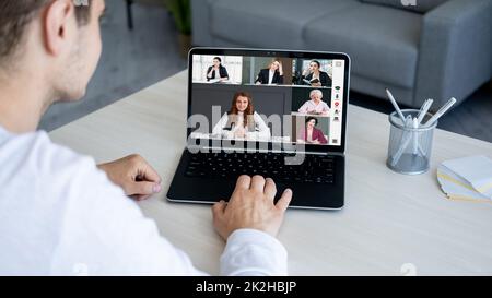 Webkonferenz. Gruppenvideoanruf. Fernkommunikation. Ein männlicher Mitarbeiter, der einen Laptop verwendet und von zu Hause aus mit einem weiblichen Geschäftsteam auf dem Bildschirm in digitaler Form arbeitet Stockfoto
