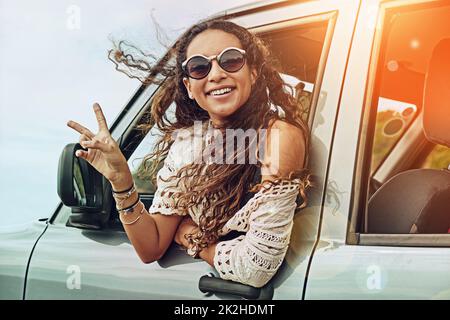 Friedliche Zeiten unterwegs. Porträt einer jungen Frau, die sich während einer Autofahrt aus dem Fenster eines Autos lehnt. Stockfoto