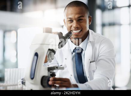 Die Welt verändern eine Entdeckung nach der anderen. Beschnittenes Porträt eines hübschen jungen Wissenschaftlers, der ein Mikroskop benutzte, während er in seinem Labor forschte. Stockfoto