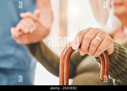 Meine Arthritis hat sich in letzter Zeit verhalten. Aufnahme einer älteren Frau, die mit Hilfe ihrer Krankenschwester einen Gehstock benutzte. Stockfoto
