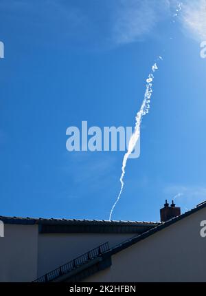 Dampfversuche, ungewöhnlich und interessant geformt, verschwinden, Locken, steigen über Dächer am Himmel auf, sehen aus wie weißer Schornsteinrauch, symbolisch Stockfoto