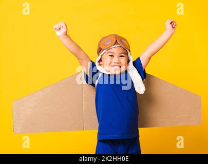 Kind kleiner Junge Lächeln tragen Pilot Hut Spiel und Schutzbrille Mit Spielzeug Pappe Flugzeug Flügel Stockfoto