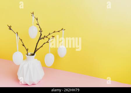 Frohe Osterferien im Frühling. Äste in weißer Vase, hängende Eier Stockfoto