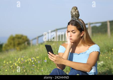 Überwältigte Frau, die mit einem Vogel auf dem Kopf telefoniert Stockfoto