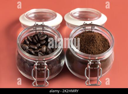 Geröstete Kaffeebohnen und gemahlener Kaffee in Glasgefäßen sind auf pinkfarbenem Hintergrund Stockfoto