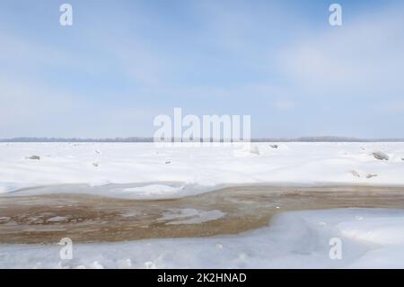 Atemberaubender Blick auf den gefrorenen Fluss bedeckt mit Eisstücken und weißem Frostschnee. Verschneite Wüste. Stockfoto