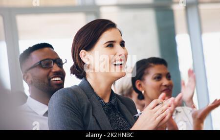 Eine kleine Aufnahme einer attraktiven jungen Geschäftsfrau, die tagsüber im Büro mit ihren Kollegen sitzt und klatscht Stockfoto