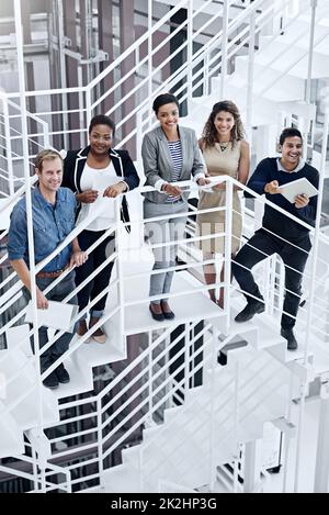 Vereint in ihrem Streben nach Erfolg. Porträt einer Gruppe lächelnder Mitarbeiter, die in einem modernen Büro auf einer Treppe stehen. Stockfoto