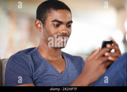 Mit einem guten Freund Schritt halten. Ein hübscher junger Mann, der sein Handy benutzt, während er sich zu Hause abkühlt. Stockfoto
