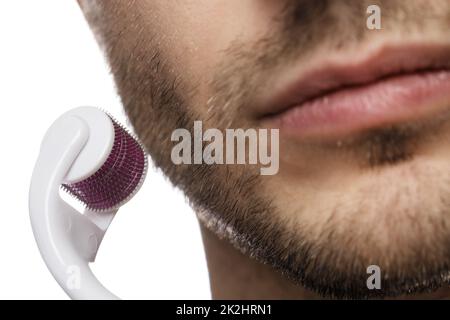 Der Mann benutzt Dermawalze für das Bartwachstum Stockfoto