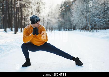 Ein sportlicher Mann, der sich vor seinem Wintertraining in einem verschneiten Park aufwärmt Stockfoto